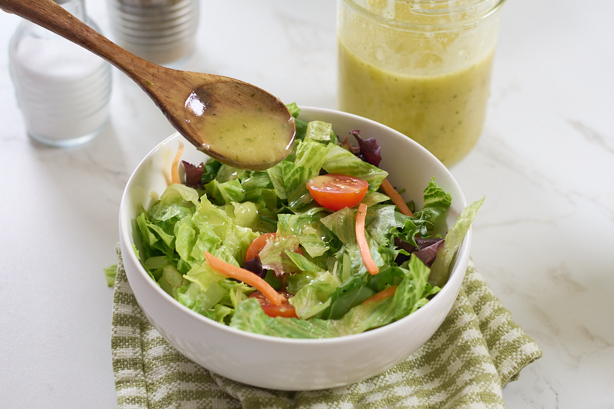 spooning dressing over bowl of salad
